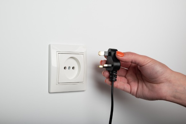 hand holding a power plug near wall outlet