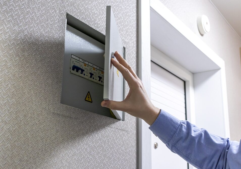 A technician inspects a residential gray metal electric breaker panel.